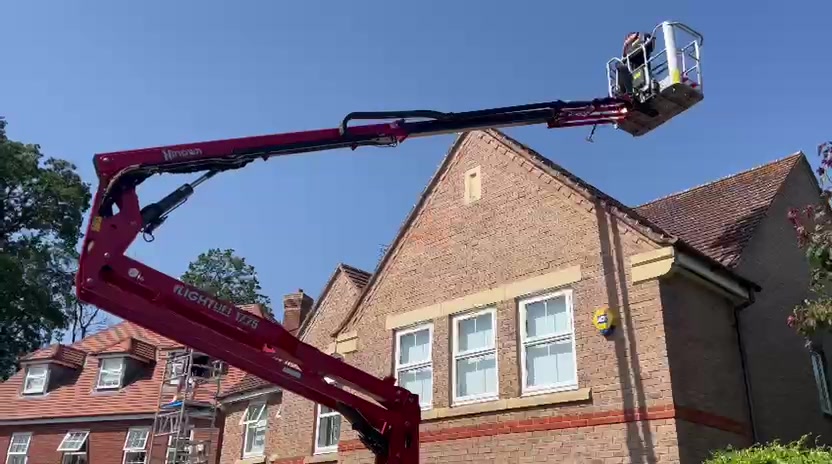 Spider lift basket reaching a residential roof gable against a clear blue sky